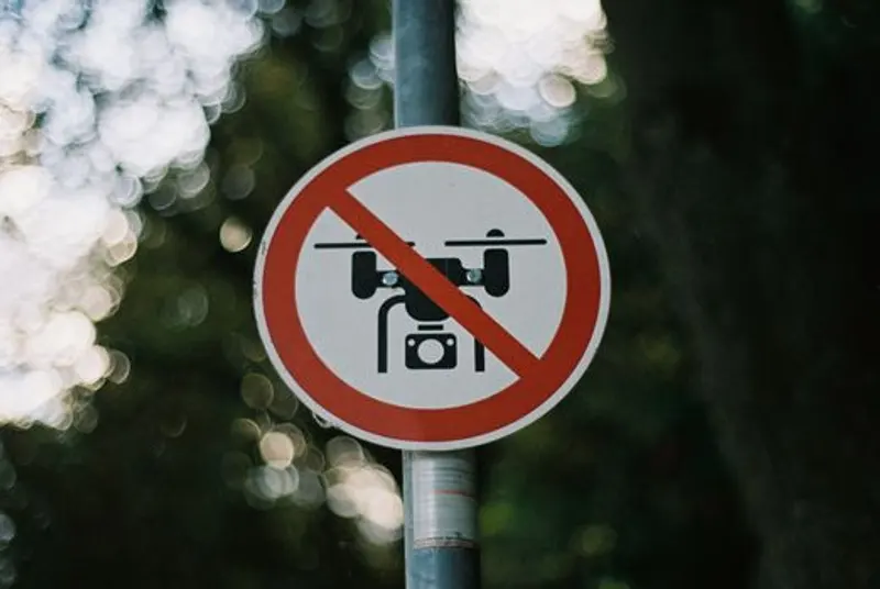 Tanda melingkar larangan drone terpasang pada tiang di hutan dengan latar belakang bokeh kabur.