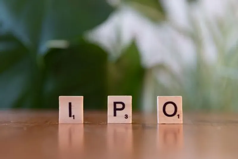 Blok huruf kayu bertuliskan IPO di atas meja, melambangkan peluang investasi.
